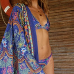 Image of a woman wearing a blue bikini and matching beachwrap. The purpose of the image is to highlight the beach cover-up by Flor Amazona.