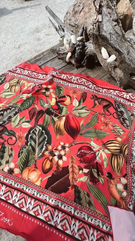 Image of a colorful cover up sitting on a wood table near the ocean. The purpose of this image is to highlight the cover up, which is made in colombia by Flor Amazona.