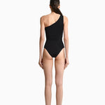  Image of the back of a woman wearing a black swimsuit with draping on the front. It's a one shoulder fit. The purpose of the image is to highlight the swimsuit because it is for sale at EVAMAIA Boutique.