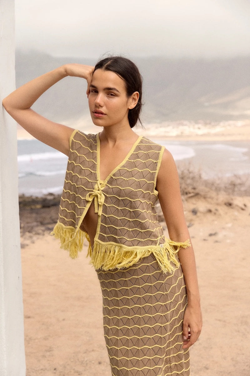 Woman wearing a yellow and brown patterned outfit on a beach.