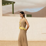 Woman in a long, patterned dress with yellow accents standing in a desert-like setting.