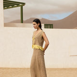 Woman in a long, patterned dress with yellow accents standing in a desert-like setting.