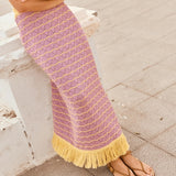 Person wearing a purple and yellow patterned skirt with tassels on a stone pavement.