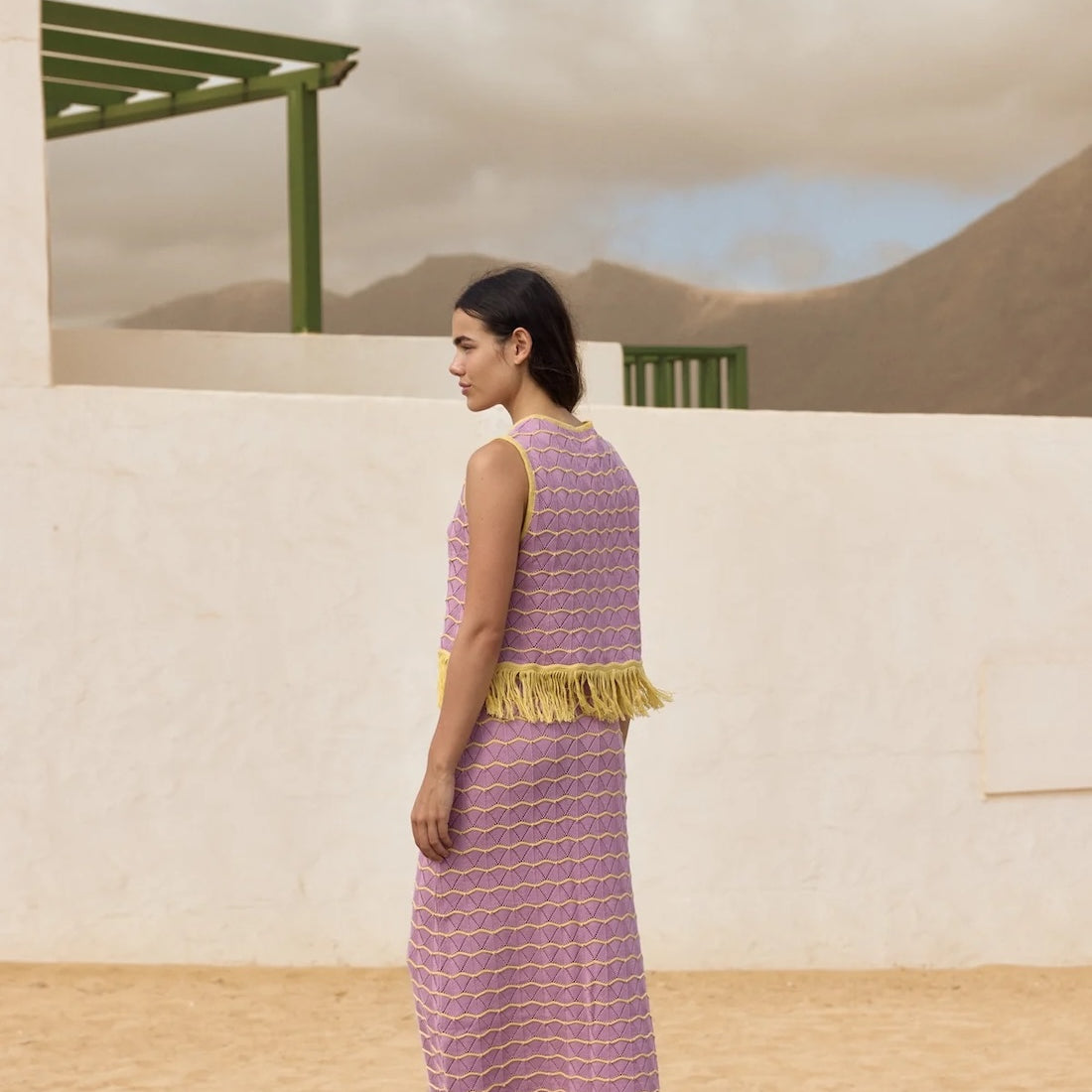Woman in a purple dress with yellow trim standing in a desert-like setting.