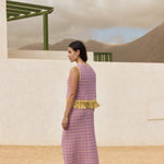 Woman in a purple dress with yellow trim standing in a desert-like setting.