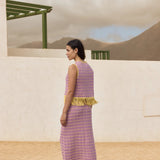 Woman in a purple dress with yellow trim standing in a desert-like setting.