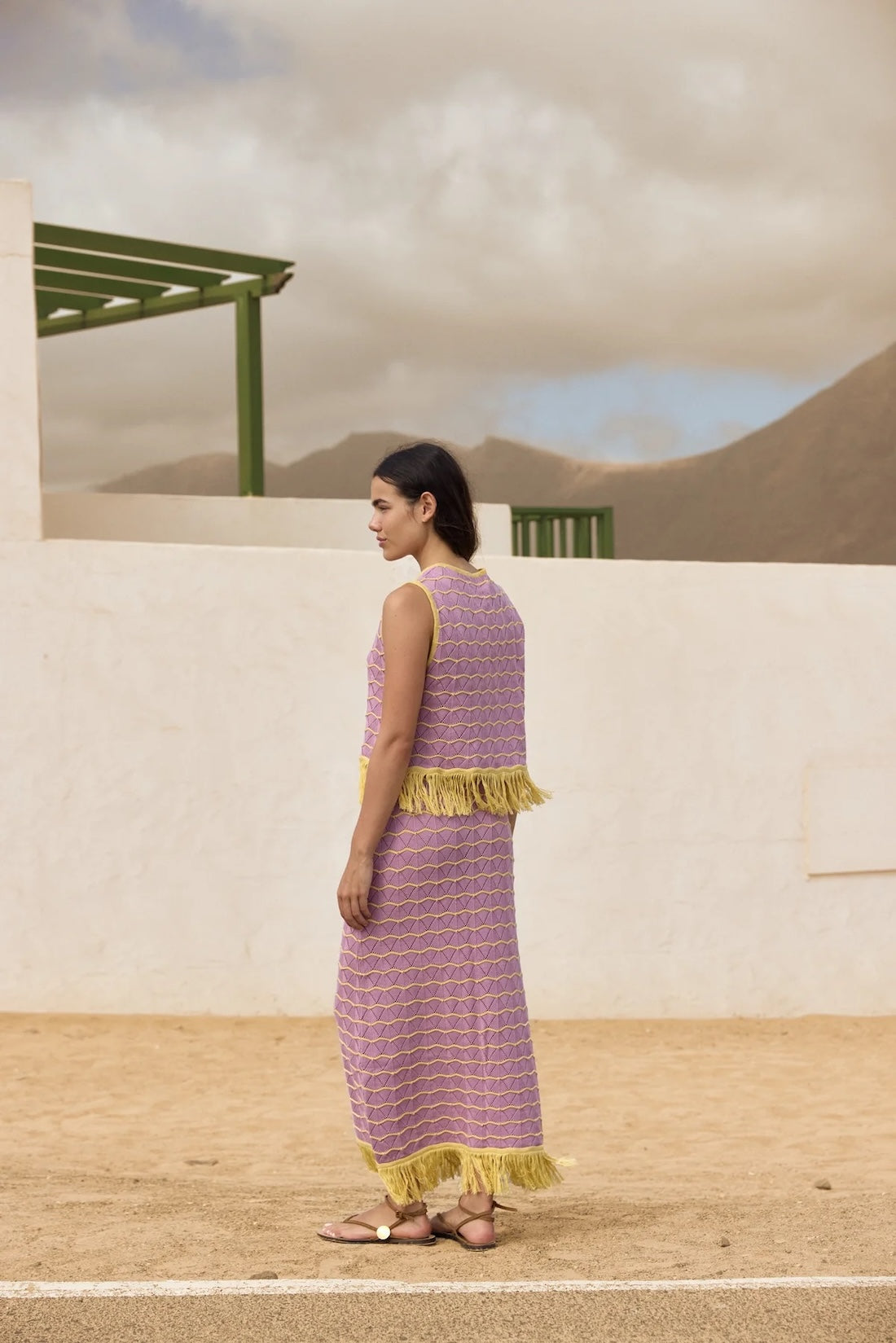Woman in a purple dress with yellow trim standing in a desert-like setting.