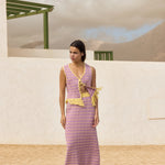 Woman wearing a pink skirt and top set with yellow accents standing in front of a white wall and green structure.