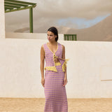 Woman wearing a pink skirt and top set with yellow accents standing in front of a white wall and green structure.