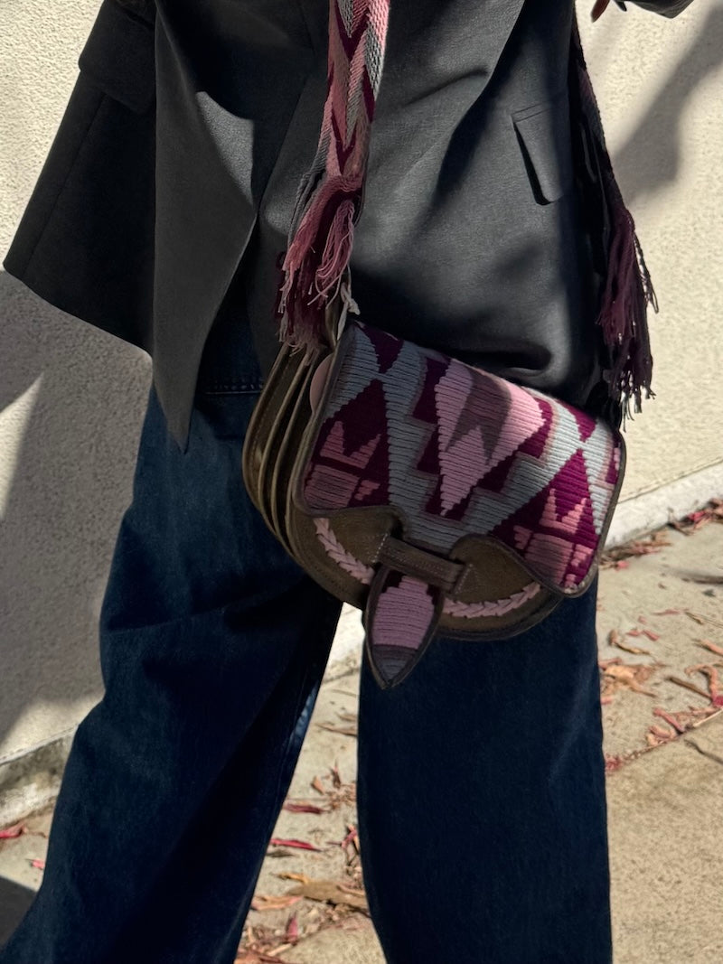 Person wearing a dark coat and jeans with a colorful patterned bag over their shoulder.