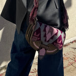 Person wearing a dark coat and jeans with a colorful patterned bag over their shoulder.