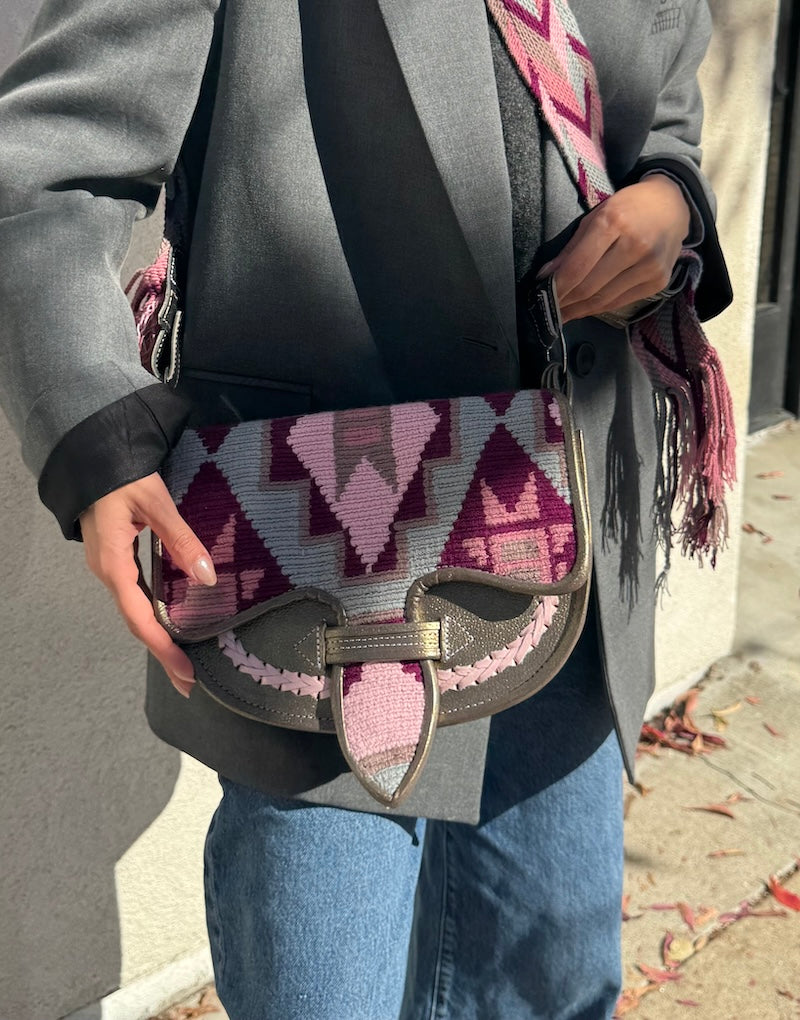 Person holding a patterned handbag with a gray coat and blue jeans.
