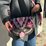 Person holding a patterned handbag with a gray coat and blue jeans.