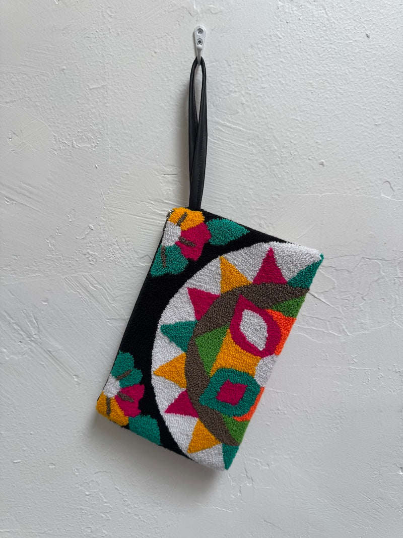 Colorful geometric patterned pouch hanging on a white textured wall.