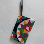 Colorful geometric patterned pouch hanging on a white textured wall.
