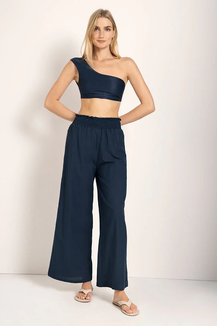 Woman wearing a bikini top with wide leg pants. She's standing against a white background and looking at the viewer. The purpose of this image is to highlight the pants.