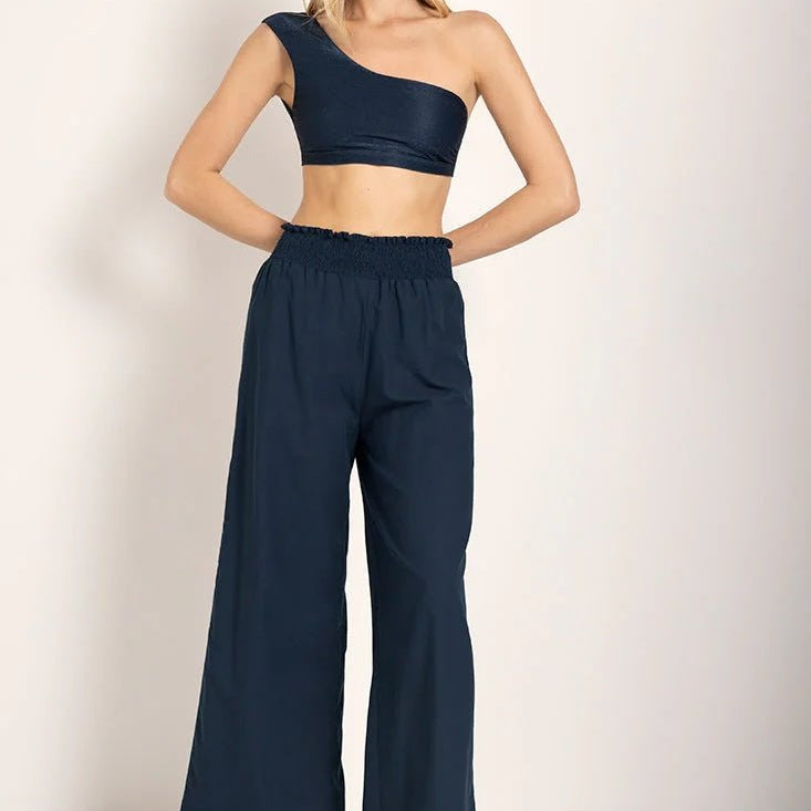 Woman wearing a bikini top with wide leg pants. She's standing against a white background and looking at the viewer. The purpose of this image is to highlight the pants.