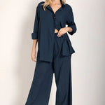 Woman wearing a button down shirt with wide leg pants. She's standing against a white background and looking at the viewer. The purpose of this image is to highlight the pants.