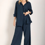 Woman wearing a button down shirt with wide leg pants. She's standing against a white background and looking at the viewer. The purpose of this image is to highlight the pants.