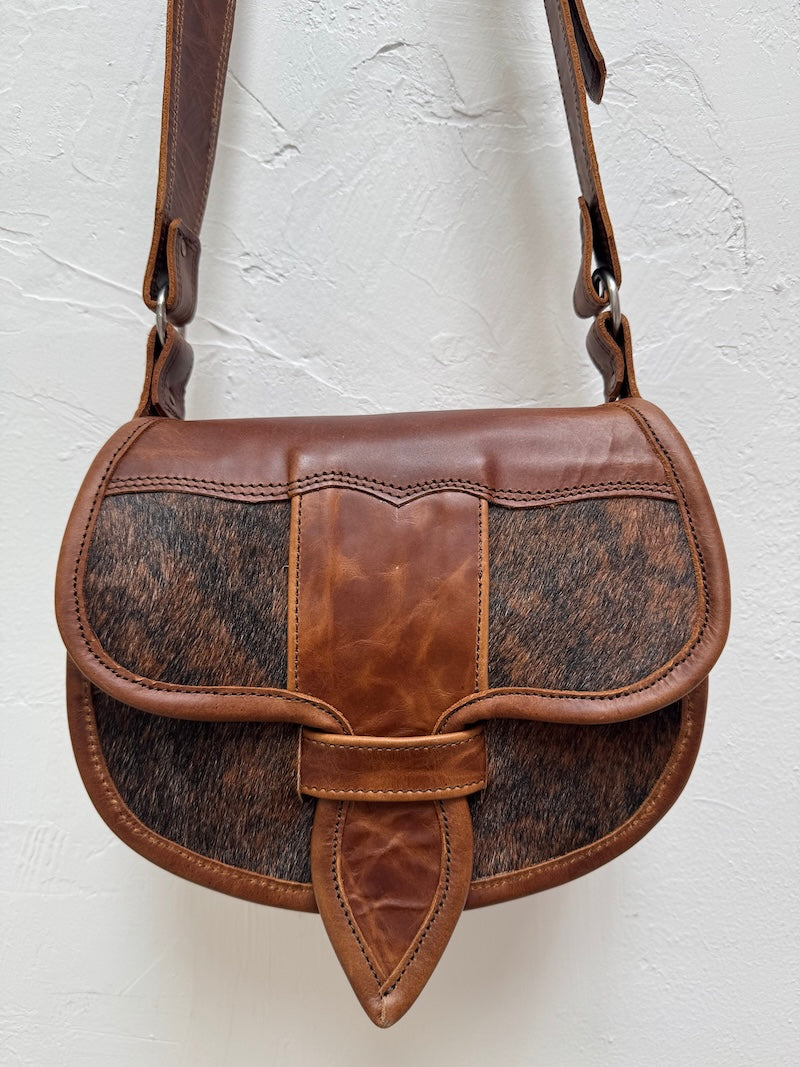 Brown leather handbag with cowhide pattern on a light gray background