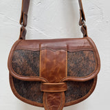 Brown leather handbag with cowhide pattern on a light gray background