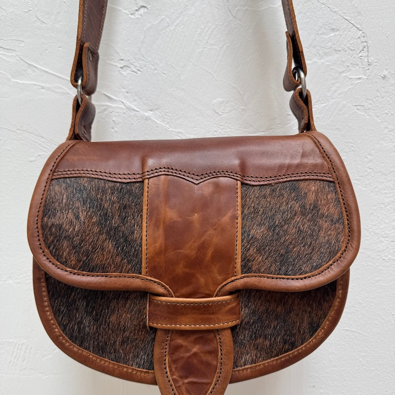Brown leather handbag with cowhide pattern on a light gray background