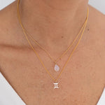 Close up image of a woman's neckline. She's wearing two necklaces. One has a charm of a Gemini zodiac sign and the other has a Moonstone. The purpose of this image is to highlight the necklaces, which are made in Colombia and sold in Studio City, at EVAMAIA boutique.