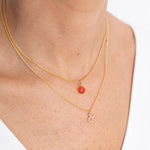 Close up image of a woman's neckline. She's wearing two necklaces. One has a charm of a Taurus zodiac sign and the other has a Coraline stone. The purpose of this image is to highlight the necklaces, which are made in Colombia and sold in Studio City, at EVAMAIA boutique.