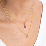 Close up image of a woman's neckline. She's wearing two necklaces. One has a charm of an aquarius zodiac sign and the other has an amethyst. The purpose of this image is to highlight the necklaces, which are made in Colombia and sold in Studio City, at EVAMAIA boutique.