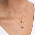 Close up image of a woman's neckline. She's wearing two necklaces. One has a charm of a Capricorn zodiac sign and the other has a smoky quartz stone. The purpose of this image is to highlight the necklaces, which are made in Colombia and sold in Studio City, at EVAMAIA boutique.