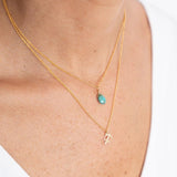 Close up image of a woman's neckline. She's wearing two necklaces. One has a charm of a Scorpio zodiac sign and the other has a Turquoise stone. The purpose of this image is to highlight the necklaces, which are made in Colombia and sold in Studio City, at EVAMAIA boutique.