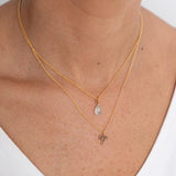 Close up image of a woman's neckline. She's wearing two necklaces. One has a charm of an Aries zodiac sign and the other has an aquamarine stone. The purpose of this image is to highlight the necklaces, which are made in Colombia and sold in Studio City, at EVAMAIA boutique.