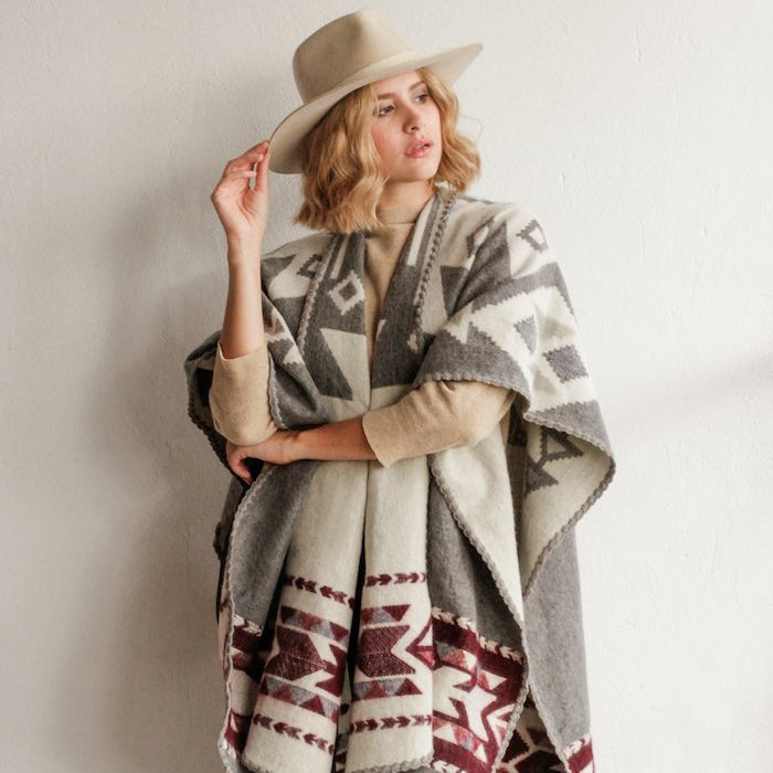 Woman wearing a hat and the Aras Poncho in Grey and Burgundy by Plisse.