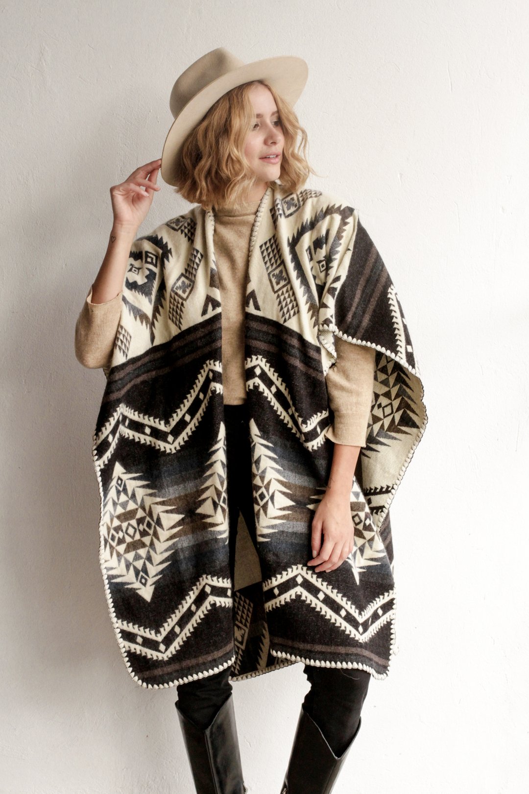 Woman modeling front of Arizona Poncho. Arizona Poncho features an overall brown themed geometric pattern all over. 