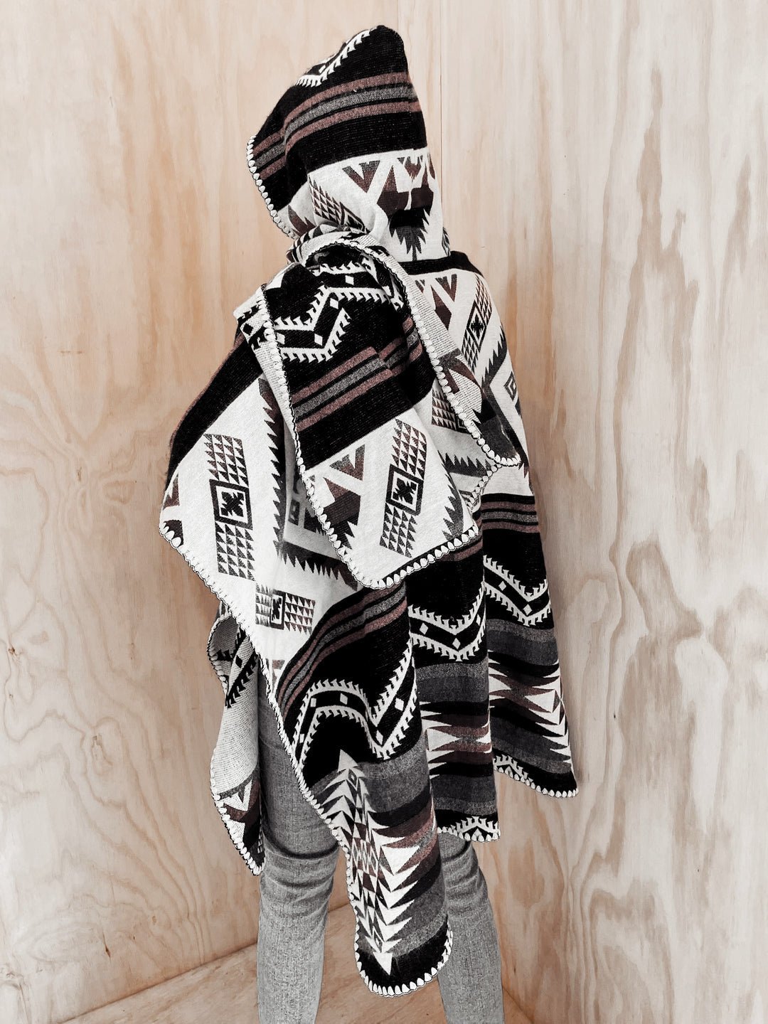 Back of the Arizona Poncho with Hood on mannequin next to natural wood walls. The poncho is paired with grey pants.