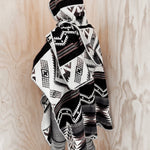 Back of the Arizona Poncho with Hood on mannequin next to natural wood walls. The poncho is paired with grey pants.