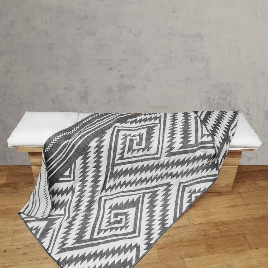 Grey El Paso Throw Blanket over displayed over bench. It is a light wash wooden bench with a white pillow top. 