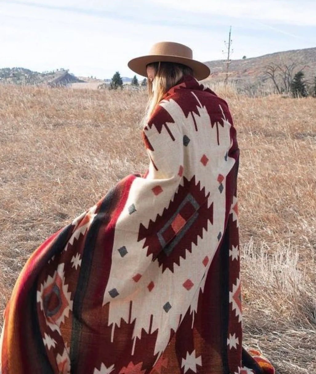 Frontera Reversible Throw Blanket draped over model. She styled it with a light brown hat. She is using the blanket outside on a field of plains.
