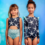 Girls' Sea Star Trikini in Deep Blue worn by little girl. She is posing in front of blue gradient background with another girl in another one piece.