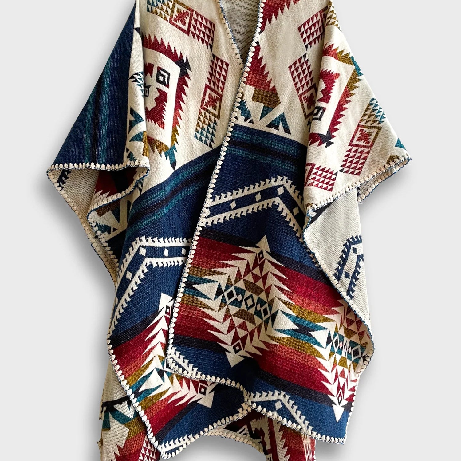 The Jalisco Poncho on a white background. It features a geometric pattern across the whole poncho with a blend of vibrant colors like black, navy blue, red, and cream.