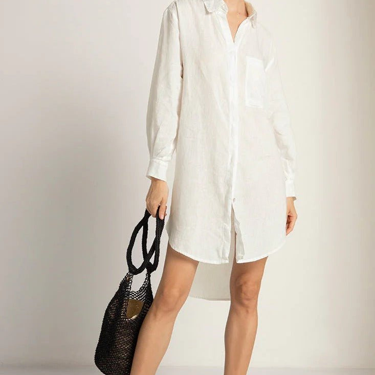 A woman wearing a long sleeved white shirt with an asymmetric hem, paired with a brown purse.
