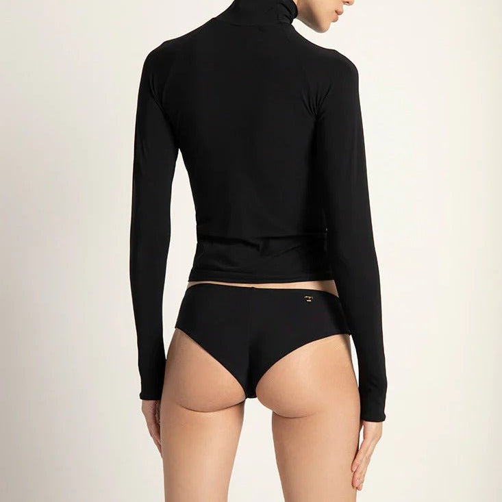A female model wearing a black long-sleeved rashguard with thumb holes and a turtleneck, paired with black bikini bottoms.