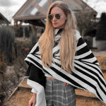 Natura Poncho by PLISSÉ. Model is wearing the poncho outside paired with grey plaid pants and sunglasses. She is standing in front of a greenhouse on a cloudy day, looking to floor.