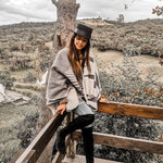 Paloma wearing grey natura poncho sitting on wooden rail. There is a view of a mountain and lots of natural plants.
