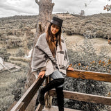 Paloma wearing grey natura poncho sitting on wooden rail. There is a view of a mountain and lots of natural plants.