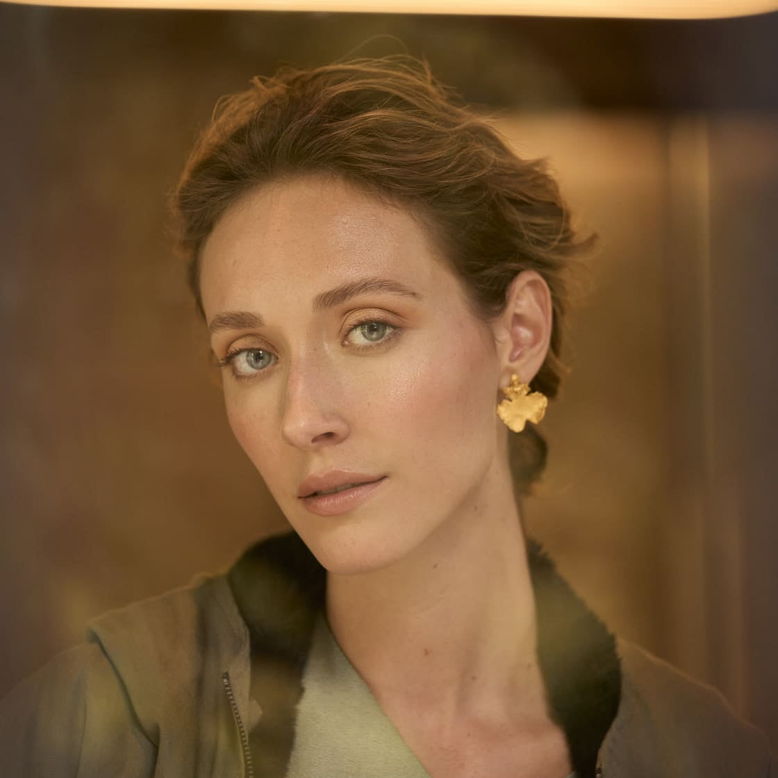 woman wearing gold orchid stud earrings by ALMA Jewelry. Available at EVAMAIA Boutique