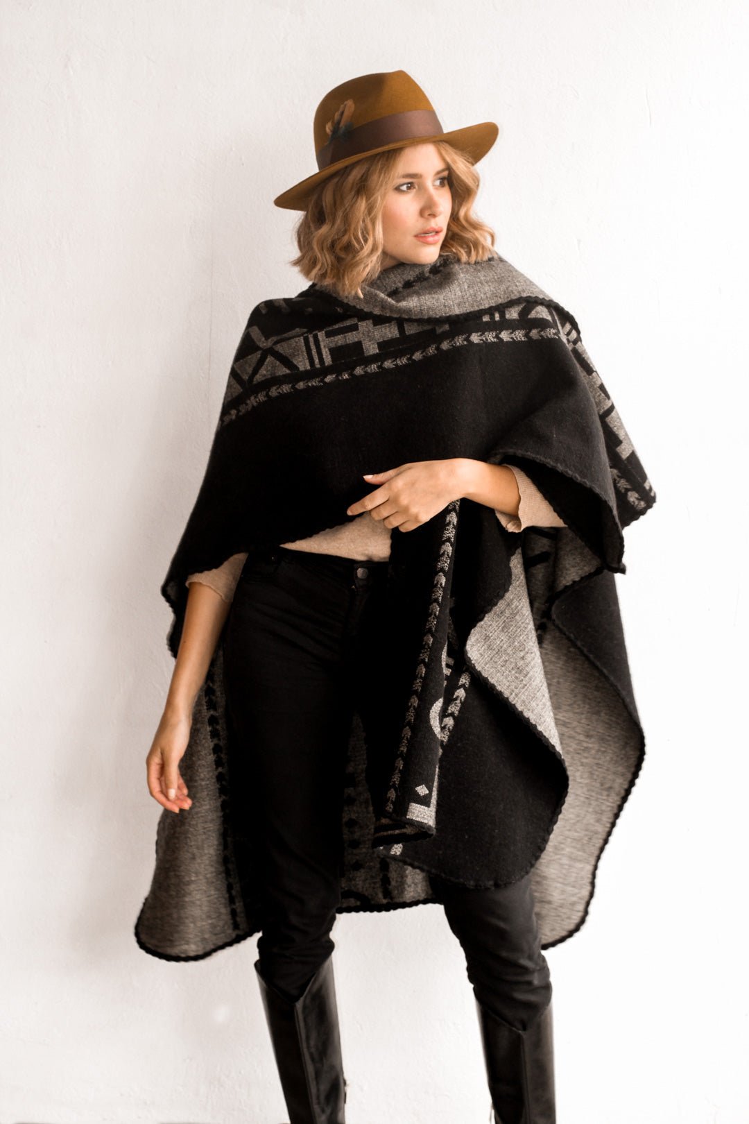 Women wearing the OX Black and Grey Poncho without the hood. She paired the poncho with a brown hat, light brown top, and black jeans.