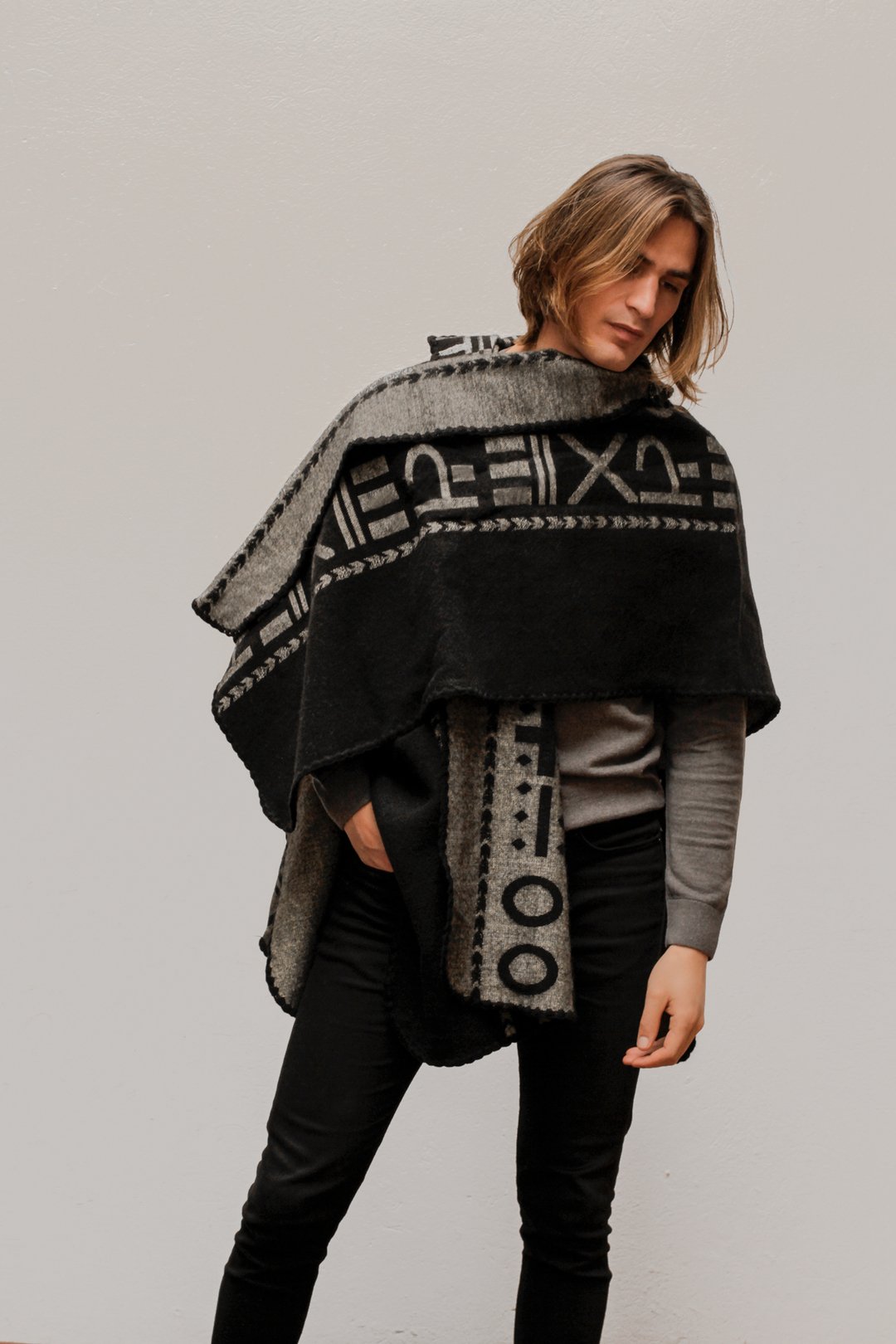 Man wearing the OX Black and Grey Poncho with Hood. He paired it with a grey top and black jeans. He is over a plain grey background.