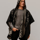 Man wearing the OX Black and Grey Poncho with Hood. He paired it with a grey top and black jeans. He is over a plain grey background.
