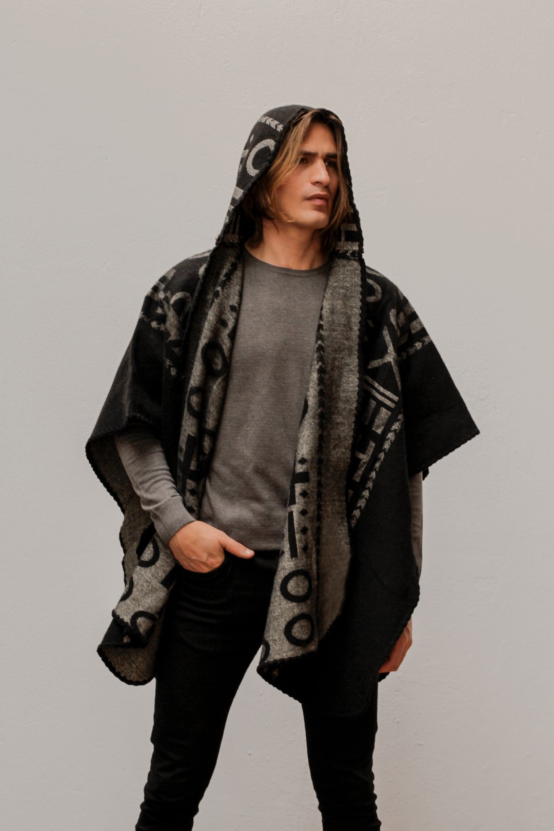 Man wearing the OX Black and Grey Poncho with Hood. He paired it with a grey top and black jeans. He is over a plain grey background.